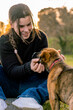 © Uri Prat - Young woman with braids in her hair petting her beloved puppy in the garden at home during sunset