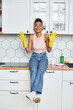 alluring jolly african american woman in homewear sitting on kitchen counter and smiling at camera