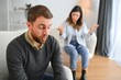Couple arguing. Wife shouting to her desperate husband sitting on a couch in the living room at home