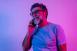 © Nenad - Pleasant news. Portrait of happy excited man joyfully looking at phone screen isolated over neon background in neon lights. Concept of human emotions, facial expression, lifestyle. Copy space for ad