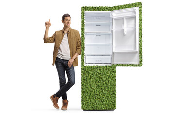 Wall Mural - Full length portrait of a casual man leaning on a power efficient fridge and pointing up