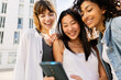 © Xavier Lorenzo - Young group of diverse girl friends watching at mobile phone screen outdoors. Millennial females having fun using smartphone together at city street.
