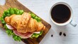 fresh croissant sandwich with ham cheese and salad leaf with coffee on white table top view