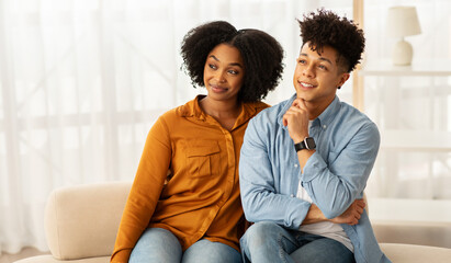 Wall Mural - A content African American couple sits closely on a sofa, the woman leaning into the man