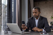 © Liubomir - Professional african american businessman using smartphone and laptop at office desk