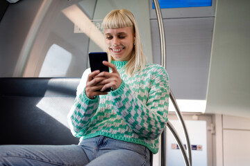 Portrait of a young woman riding in a train or a subway and using a phone