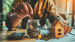Close up of man hand putting coin into glass jar with house model and calculator on wooden table background