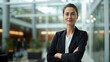 © Road Red Runner - Caucasian businesswoman confidently poses with her arms crossed in front of a modern building.