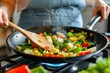 © VolumeThings - Woman cooking vegetables in wok on gas stove in kitchen