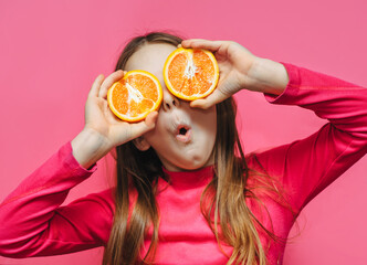 Little cute funny girl using grapefruit instead of eyes, having fun and fooling around in the studio on a pink background. Concept of citrus diet, fruits and vitamins.