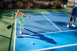 © joescarnici - A woman in green plays pickleball with a big shadow on a blue court