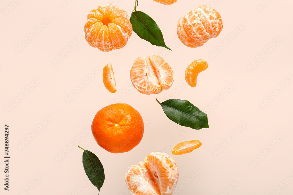 Flying sweet ripe mandarins and leaves on beige background