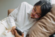 Side view of asian Thai office woman wear glasses using mobile phone while leaning and resting on brown couch sofa, tired of work. 