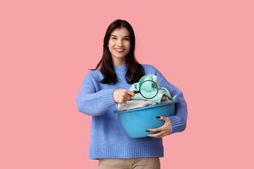 Sticker - Beautiful young woman holding basket with clean laundry and magnifier on pink background