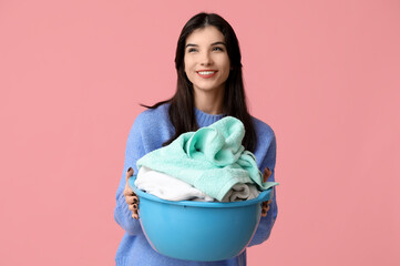 Sticker - Happy young woman holding basket with clean laundry on pink background