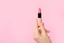 Hand holding lipstick on pink background
