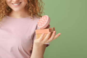 Young woman with hair scalp massager and shampoo bars on green background