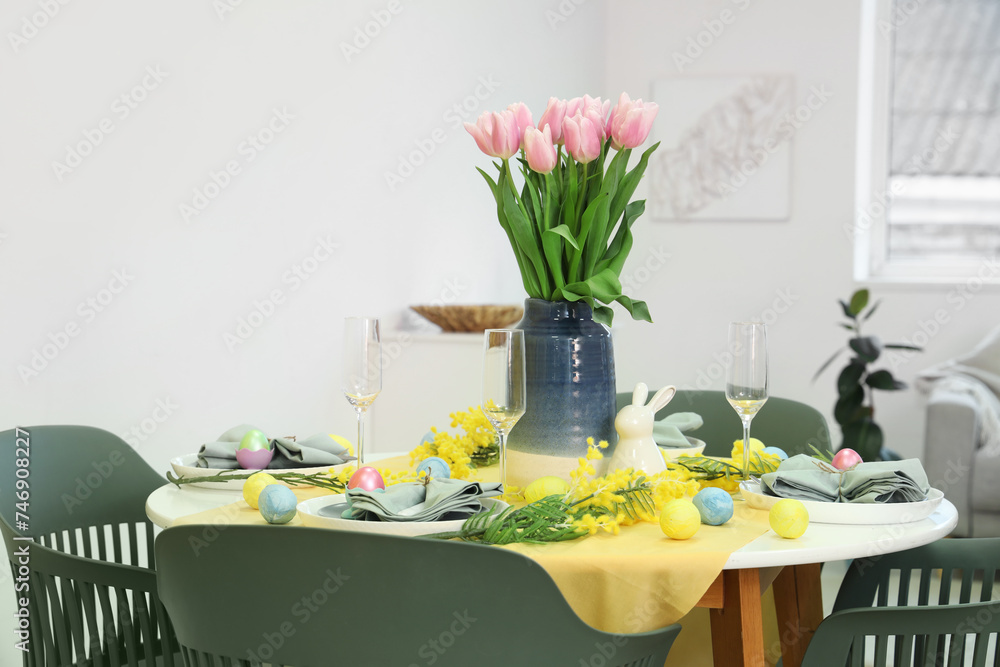 Festive Easter table setting with vase of tulips, mimosa flowers and painted eggs