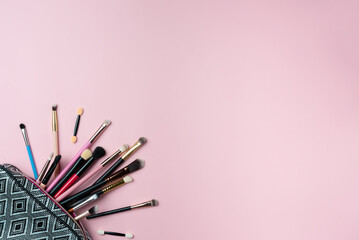 Wall Mural - Makeup brushes falling out of cosmetics on pink background