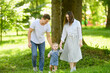 © GRON777 - Child takes his first steps in the park on the grass, holding hands with his parents, learning to walk independently. Concept of family, family vacation in nature, first steps