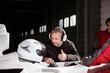 © Image Source - Race team strategist giving a thumbsup as he communicates over the headset, with a racing car and driver in the background.