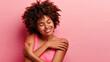 © KidSpace - Self care and love concept. Happy African American woman portrait hugging herself with pink background