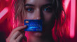 Close-up of a woman holding a credit card near her face with neon lights in the background.