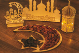 Fototapeta  - Ramadan Kareem. Dates on wooden tray in the shape of a month and a star and oriental wooden Lantern lamps on wood background. Islamic Holy Month Greeting Card. Soft focus. Shallow DOF.