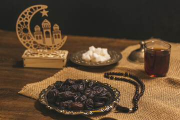 Wall Mural - Glass of tea with sugar and dried dates on a wooden background with burlap. Ramadan Kareem holiday background. Halal meal set for fasting is obligatory for Muslim on wooden.  Soft focus. Shallow DOF.
