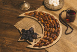 Fototapeta  - Dried dates on a tray in the shape of a month and a star with tea and sugar cubes on a wooden background with burlap. Ramadan Kareem holiday background.  Soft focus. Shallow DOF.
