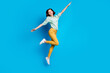 Full length photo of girlish woman dressed teal shirt yellow trousers jumping hold arms like wings isolated on blue color background