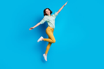 Canvas Print - Full length photo of girlish woman dressed teal shirt yellow trousers jumping hold arms like wings isolated on blue color background