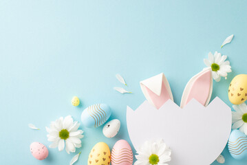 Wall Mural - Whimsical Easter imagination concept. Top view of cute bunny ears visible through split egg, with chamomiles and multicolored eggs on sky-blue surface, providing area for special messages or advert