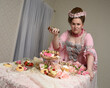 Close up portrait of cute female model wearing an opulent pink gown, the costume of a historical French baroque nobility.  sitting at table with sweet cakes and indulgent food feast.