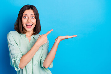 Wall Mural - Photo of impressed woman dressed turquoise shirt indicating at awesome product on palm empty space isolated on blue color background