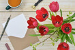 Bunch of red tulips, blank sheet of paper, envelope, teacup, pen on wooden table. Shallow depth of field, Flat lay. 