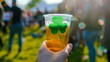 Hand holding a plastic beer cup with green shamrock symbol at street open-air festival of celebration of St. Patrick's Day	