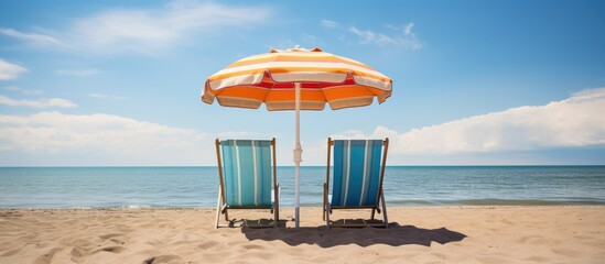 Canvas Print - Two beach chairs are arranged under a large umbrella on a sandy beach. The chairs face the ocean, with gentle waves lapping against the shore. The scene is inviting and perfect for relaxing in the sun