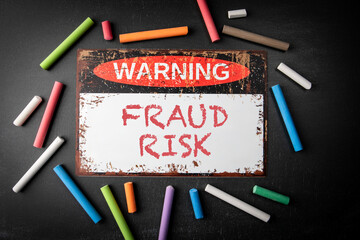 Wall Mural - Fraud Risk. Metal warning sign and colored pieces of chalk on a dark chalkboard background