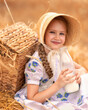 A portrait of a happy girl in a wheat field at sunset. A child holds a glass jar with milk against the background of rye ears.
