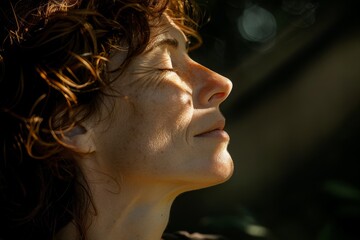  Close-up of a curly-haired woman with a peaceful expression, immersed in natural sunlight filtering through the foliage.