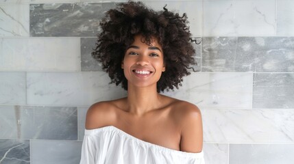 Wall Mural - A joyful woman with curly hair wearing a white off-the-shoulder top smiling against a marble tile wall.