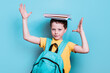 © ADDICTIVE STOCK - A school boy with a backpack strikes a playful pose, balancing a stack of books on his head against a light blue background
