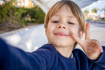 Cute little smiling boy taking a selfie with peace symbol outdoor