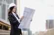 © Nassorn - Architect designer working outside on real estate apartment layout in downtown. Female property development engineer in suit reading housing sketch blueprint of building. Young adult professional job.