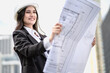 © Nassorn - Architect designer working outside on real estate apartment layout in downtown. Female property development engineer in suit reading housing sketch blueprint of building. Young adult professional job.