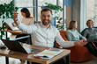 © standret - Cheerful friendly man is sitting by the table with laptop. People are working in the office with bean bags chairs in it