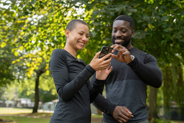 Wall Mural - Smiling athletic man and woman looking at smart phone in park