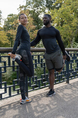 Wall Mural - Athletic man and woman stretching legs on bridge in park