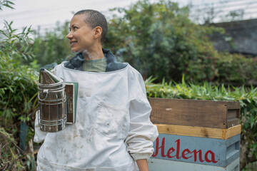 Wall Mural - Smiling female beekeeper holding smoker in urban garden